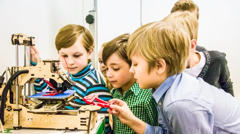 Drei Kinder studieren einen 3D-Drucker