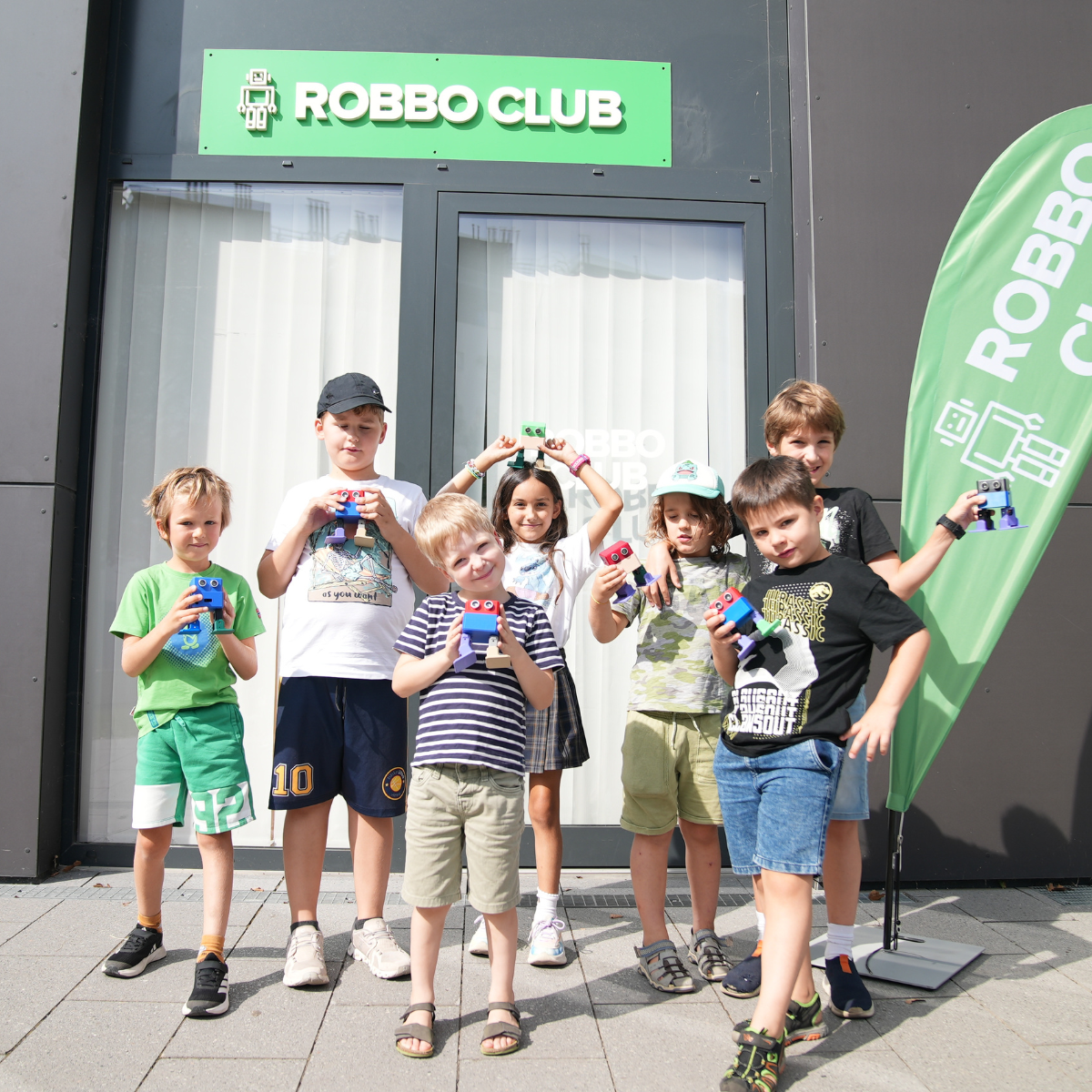 Kinder präsentieren stolz ihre Roboter vor dem Robbo Club Gebäude.