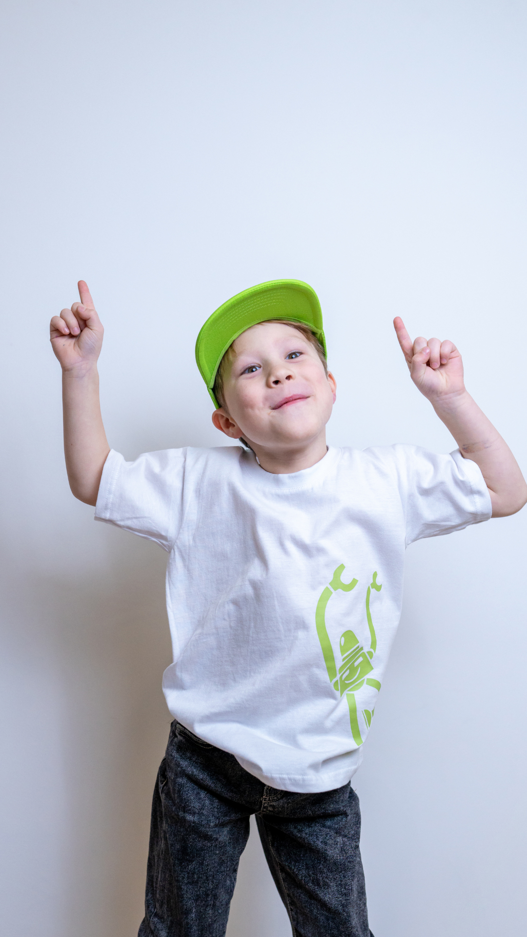 Ein fröhliches Kind in einem Robbo-T-Shirt und einer grünen Kappe zeigt mit beiden Händen nach oben.