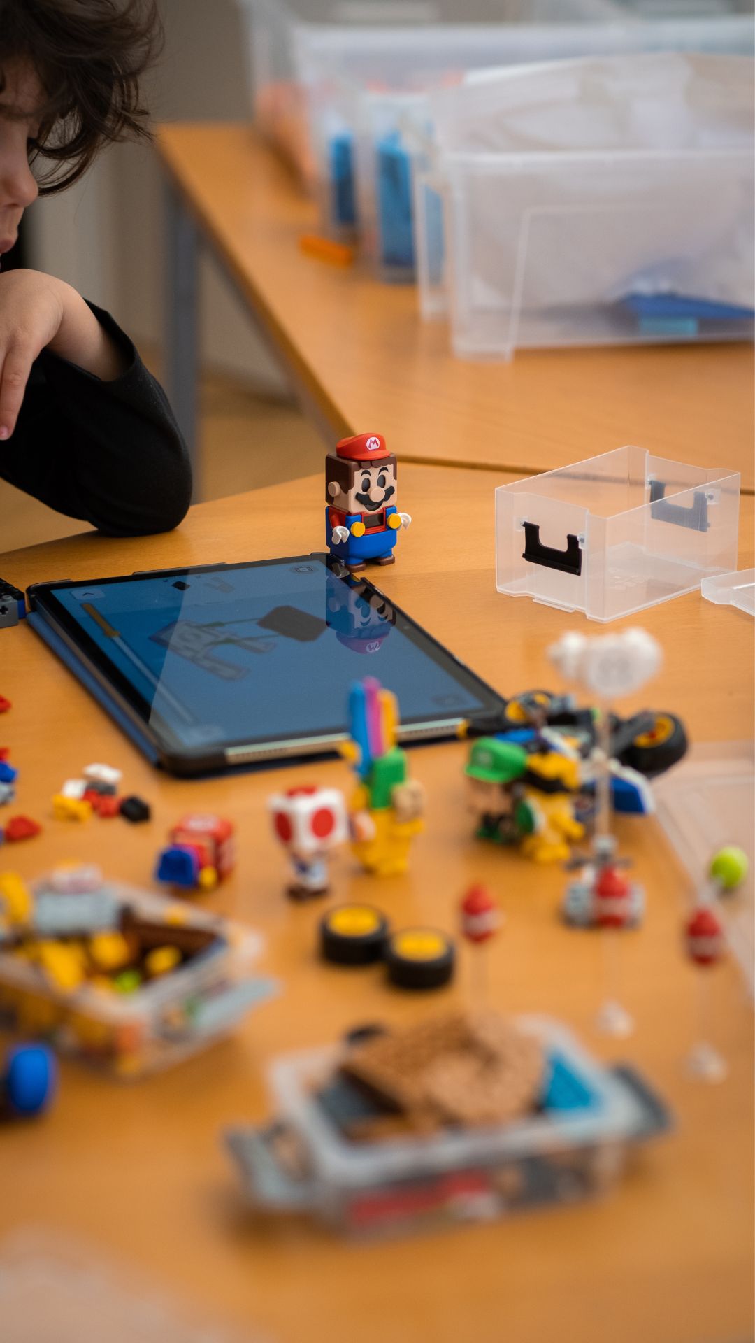 Kind arbeitet mit Lego Super Mario Figuren und Tablet im Workshop