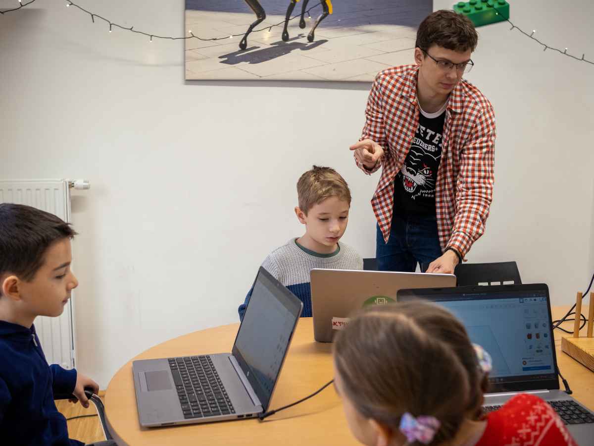 Trainer erklärt einem Kind den nächsten Schritt im 3D-Workshop.