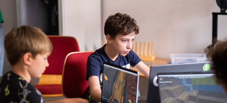 Kinder spielen und programmieren Minecraft beim Robbo Club Kindergeburtstag und arbeiten konzentriert an ihren Laptops.