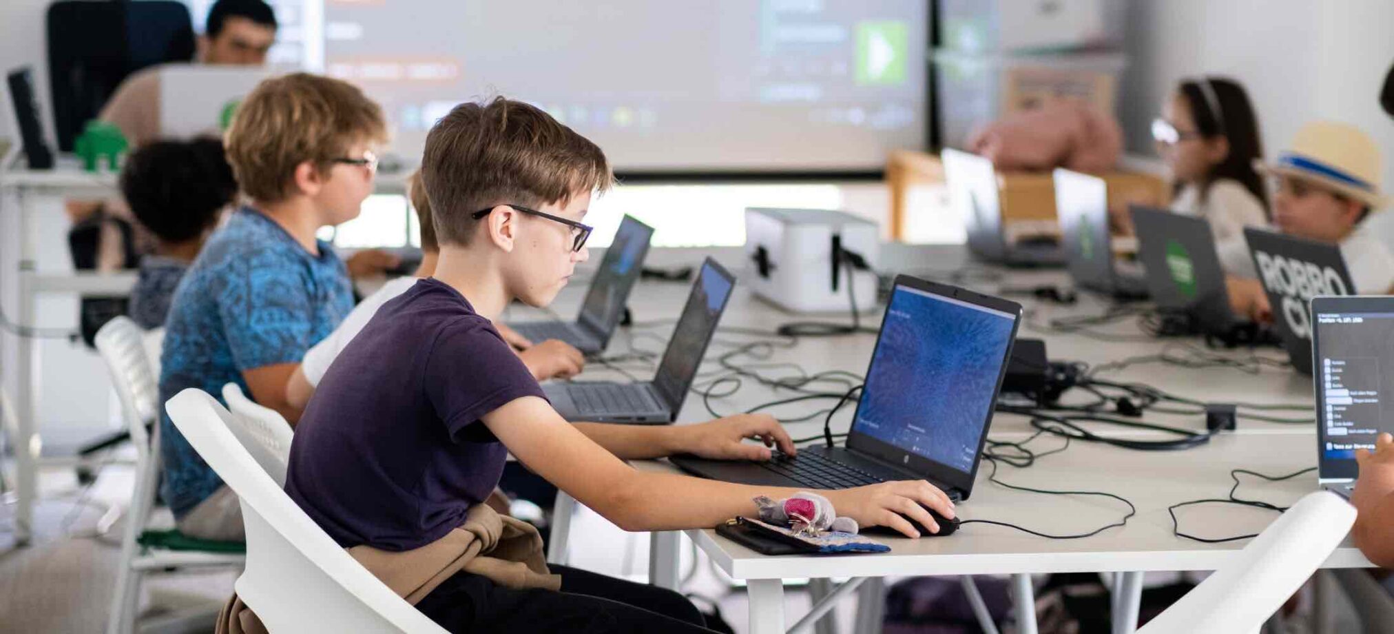 Kinder und Jugendliche arbeiten konzentriert an Laptops während eines Robbo Club Kurses.