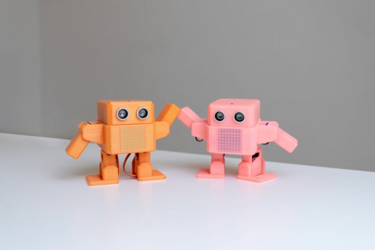 Zwei kleine Roboter mit Teilen aus dem 3D-Drucker, einer orange und einer rosa