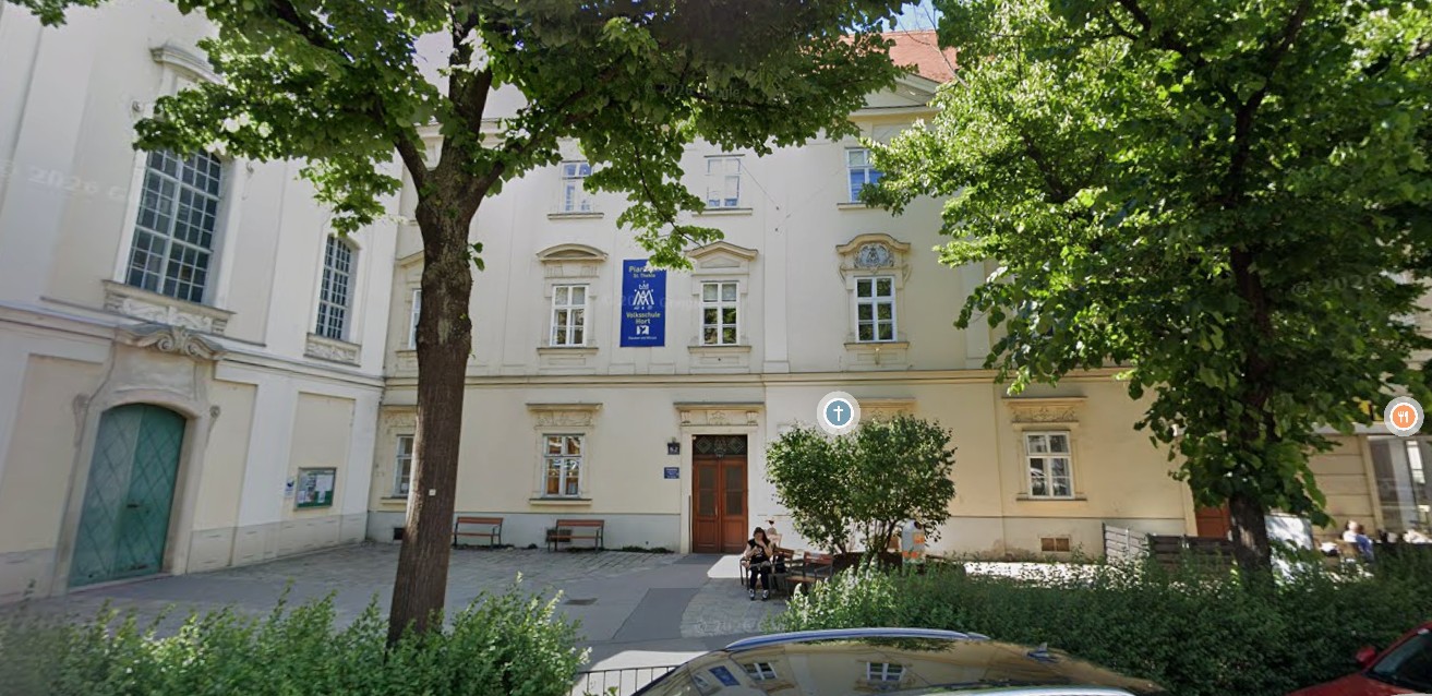 Klassizistisches Schulgebäude mit beiger Fassade und großem Baum im Schulhof