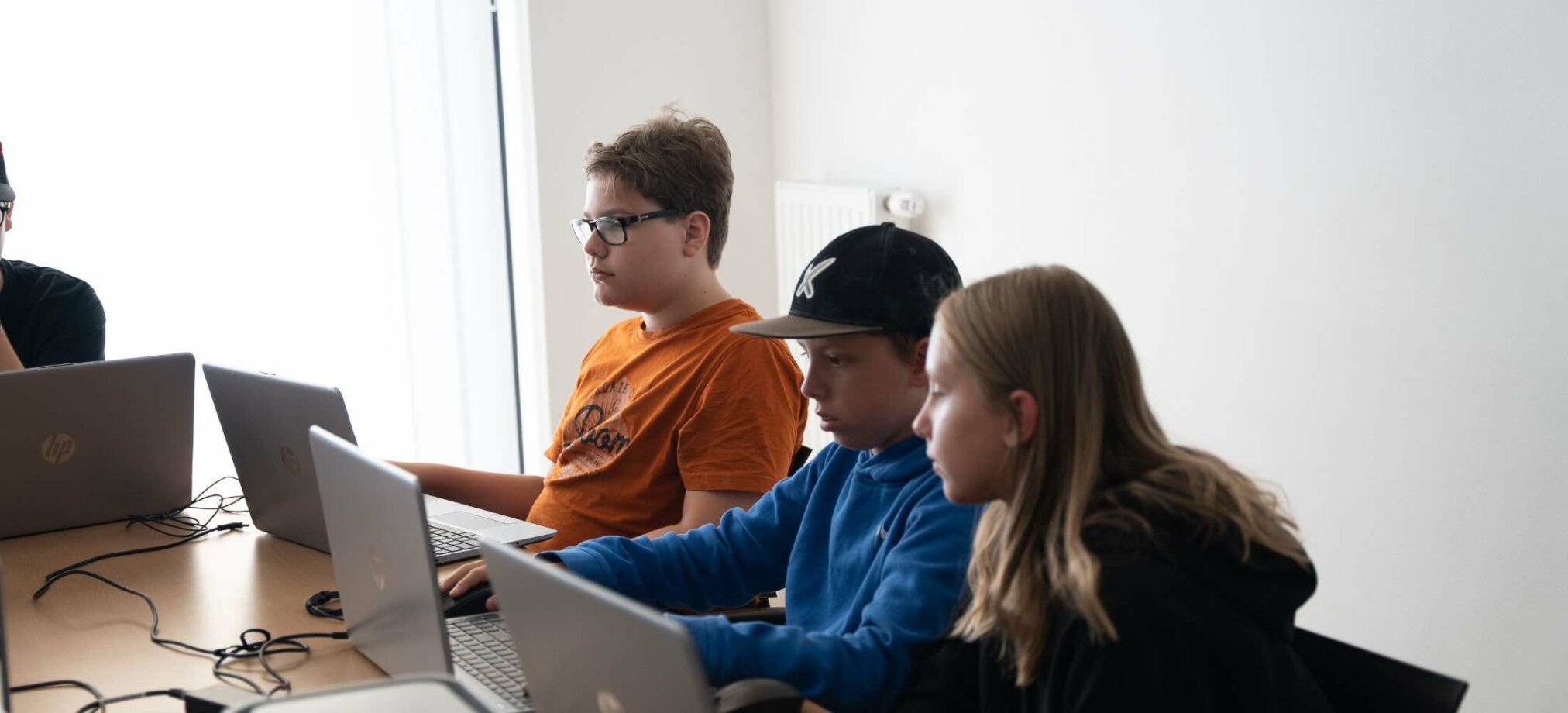 Drei Jugendliche sitzen im Robbo Club vor ihren Laptops und arbeiten konzentriert an einem Programmierprojekt während eines 14. Geburtstags.