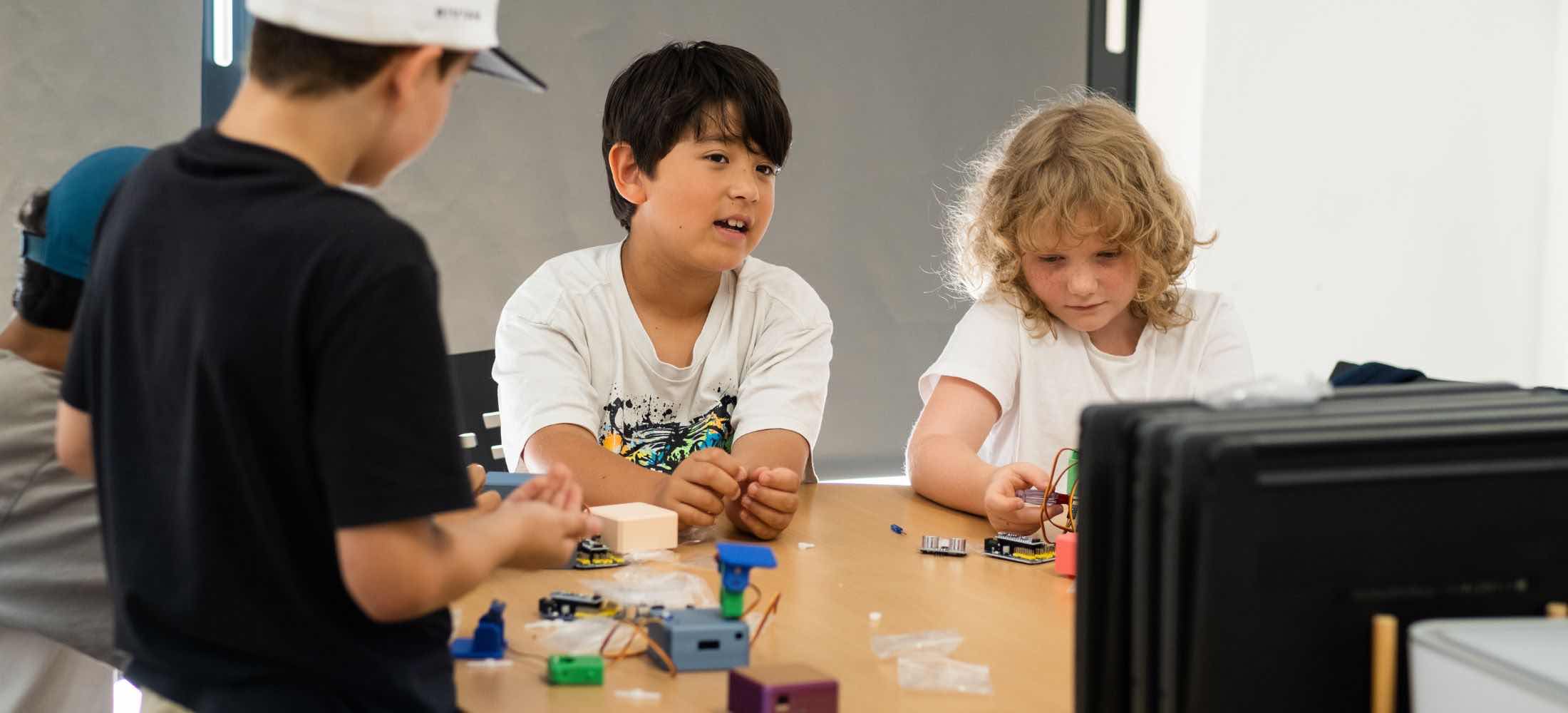 Kinder im Alter von etwa sieben Jahren arbeiten gemeinsam im Robbo Club an kleinen Robotik-Projekten.