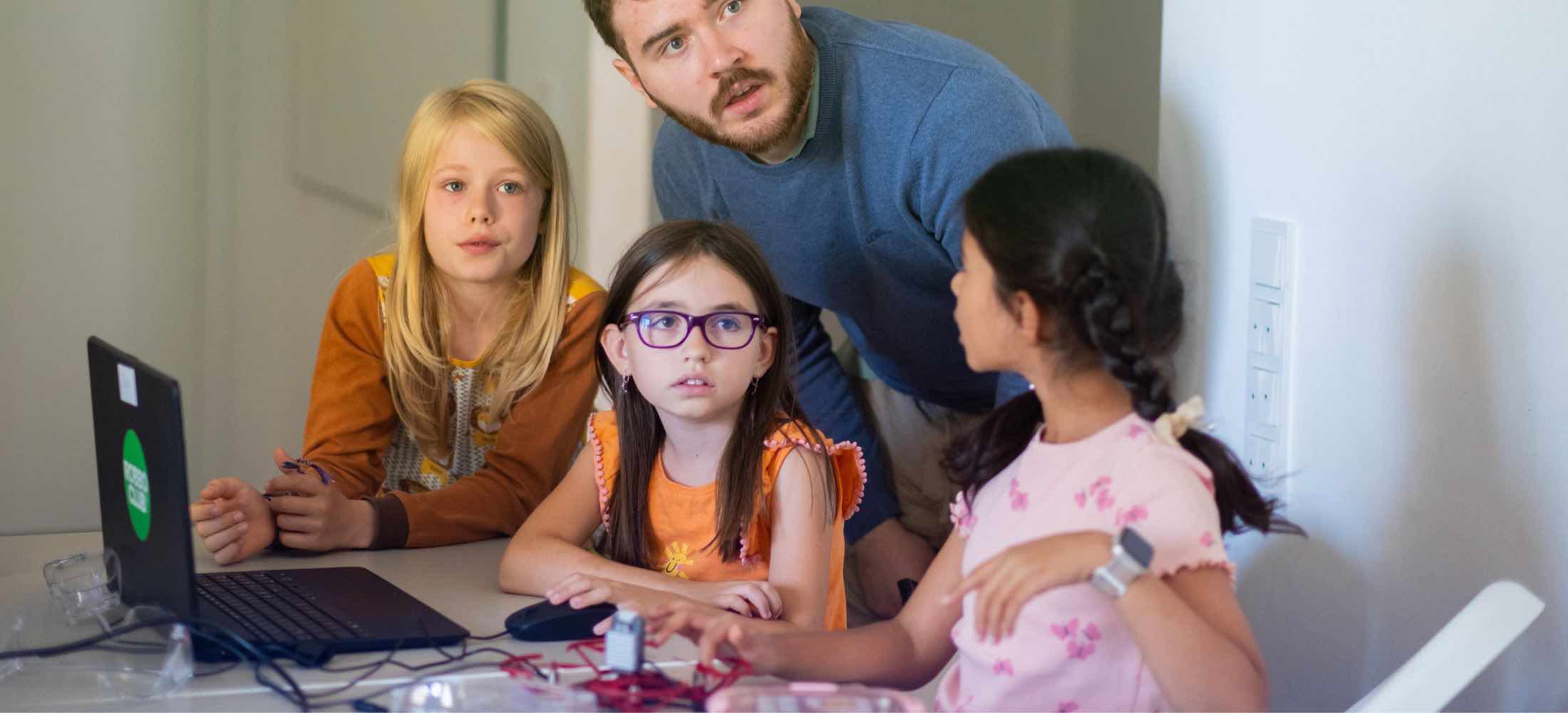 Gruppe von achtjährigen Kindern arbeitet im Robbo Club gemeinsam am Computer, unterstützt von einem Trainer.