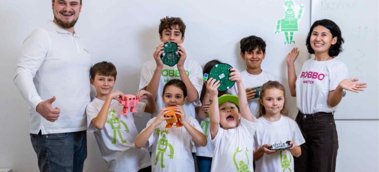 Gruppe hochbegabter Kinder im Robbo Club zeigt stolz selbstgebaute Roboter und Elektronikprojekte, begleitet von zwei Lehrkräften.