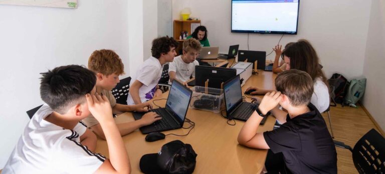 Eine Gruppe Jugendlicher arbeitet im Robbo Club konzentriert an Laptops, während ein Trainer vorne Inhalte zur KI und Robotik erklärt.