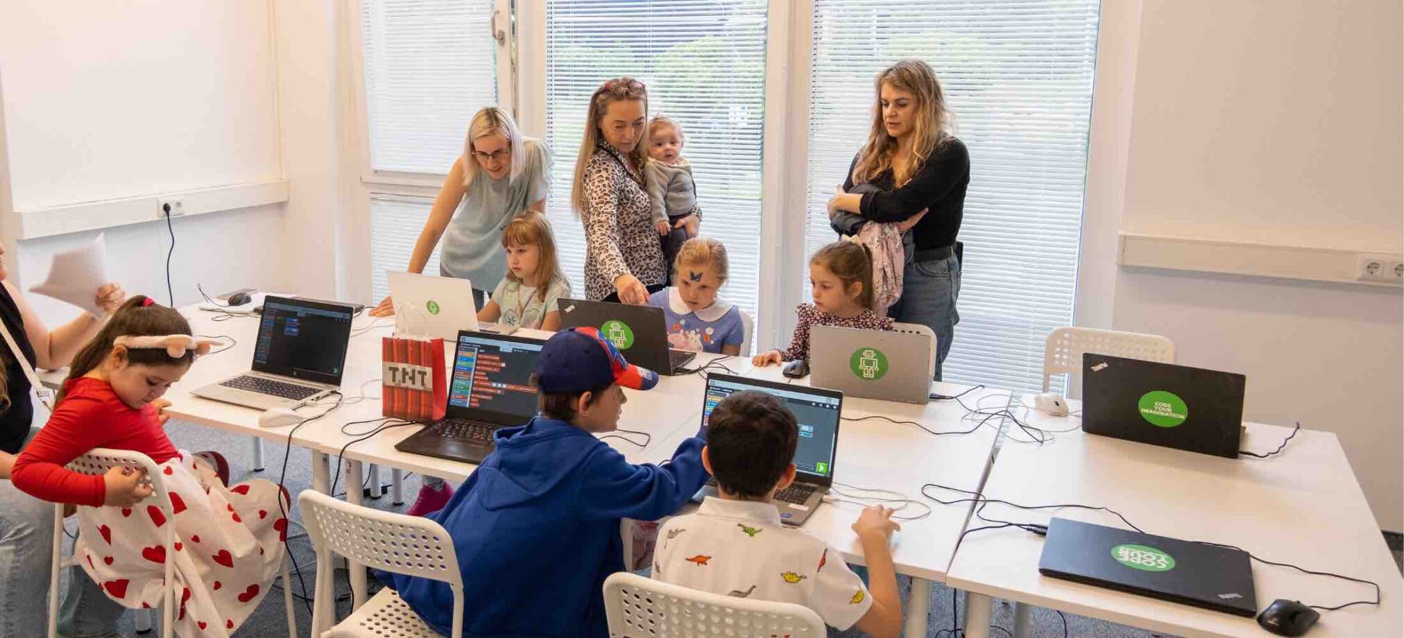 Kinder feiern im Robbo Club im 23. Bezirk einen Geburtstag und programmieren gemeinsam an Laptops, begleitet von Erwachsenen.