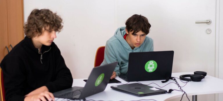 Zwei 15-jährige Jugendliche arbeiten konzentriert an Laptops im Robbo Club Unterrichtsraum.