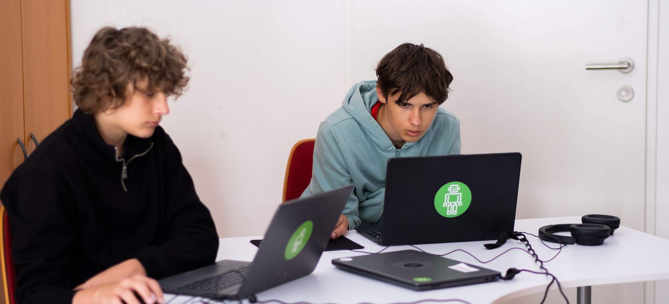 Zwei 15-jährige Jugendliche arbeiten konzentriert an Laptops im Robbo Club Unterrichtsraum.