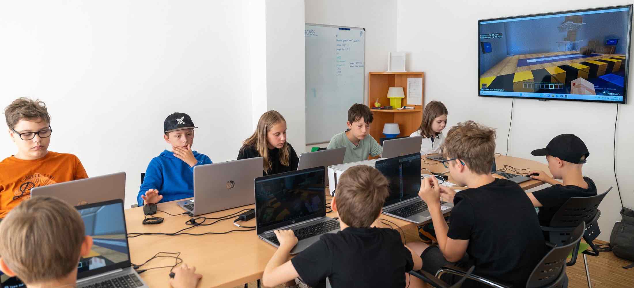 Kinder sitzen mit Laptops im Unterricht und programmieren Minecraft-Welten, während eine große Bildschirmanzeige das Spiel zeigt.