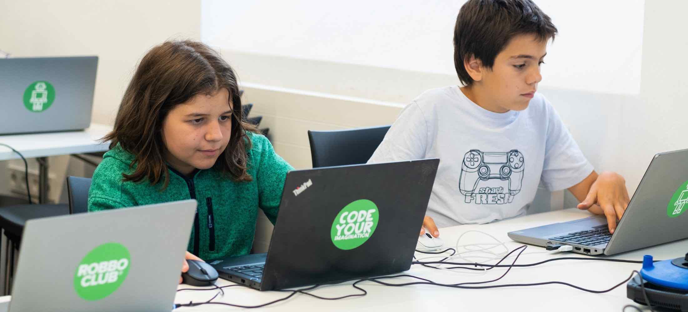 Kinder lernen im Robbo Club die Grundlagen von Python und programmieren konzentriert an ihren Laptops.