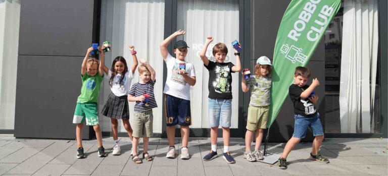 Gruppe von jungen Kindern vor dem Robbo Club, die stolz ihre selbstgebauten Roboter präsentieren.