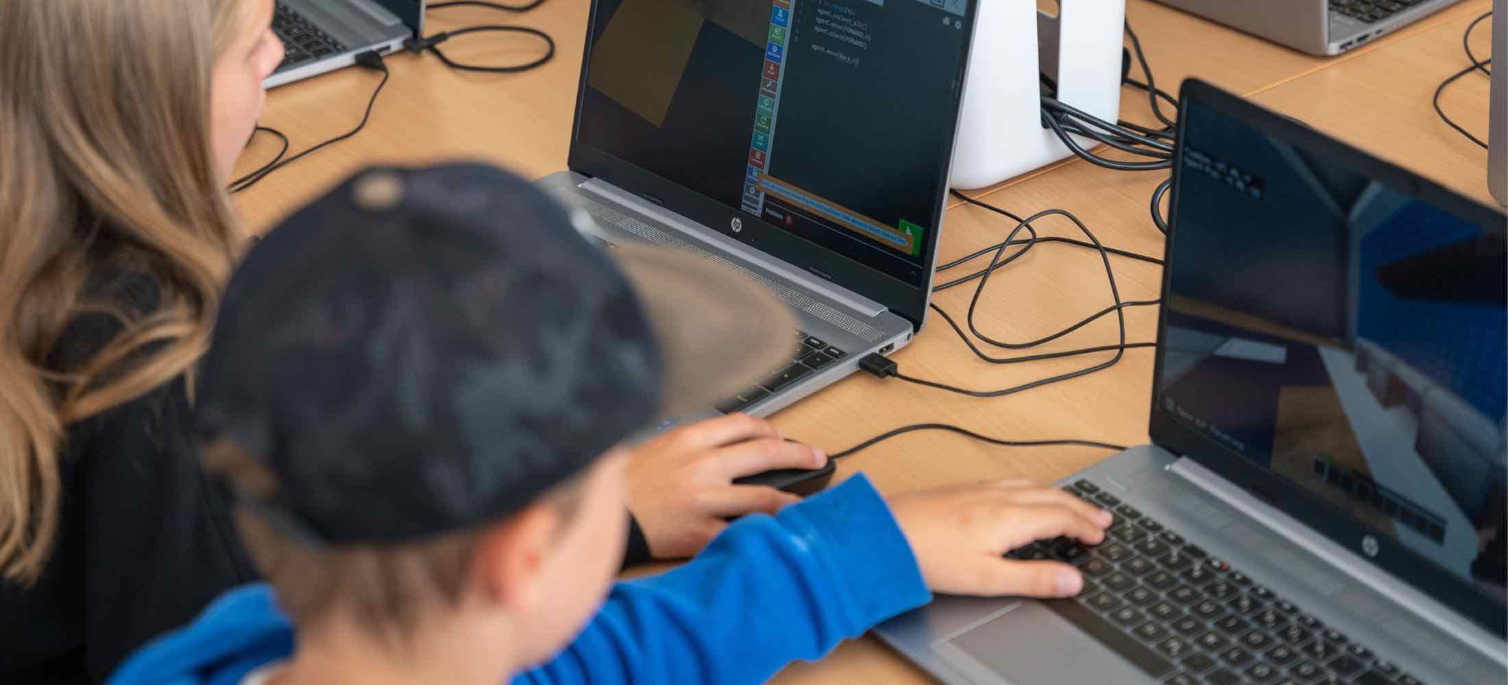Kinder im Alter von 8 bis 12 Jahren programmieren Minecraft am Laptop und arbeiten konzentriert an ihren Coding-Projekten.