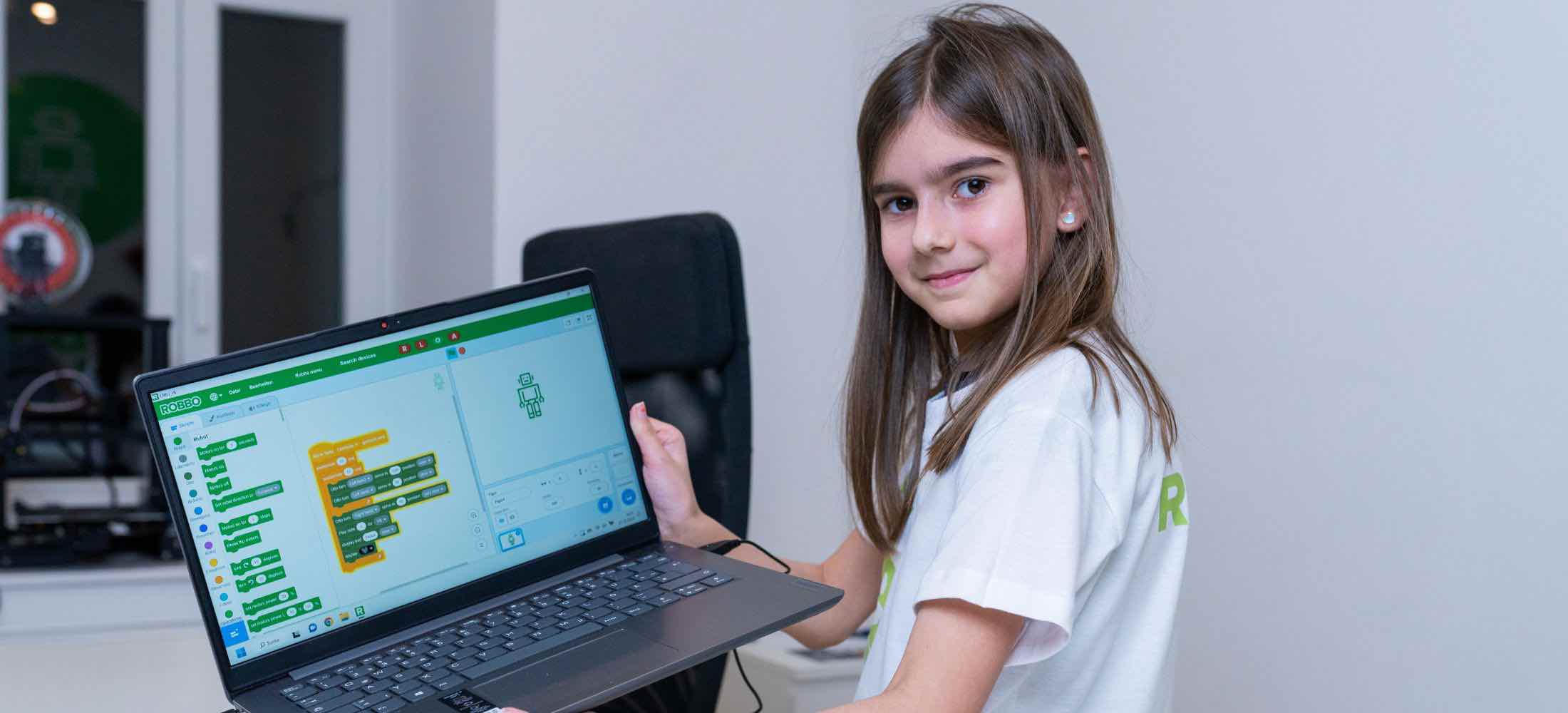 Mädchen zeigt stolz am Laptop ihr selbst erstelltes Programm in der visuellen Robbo-Programmierumgebung.