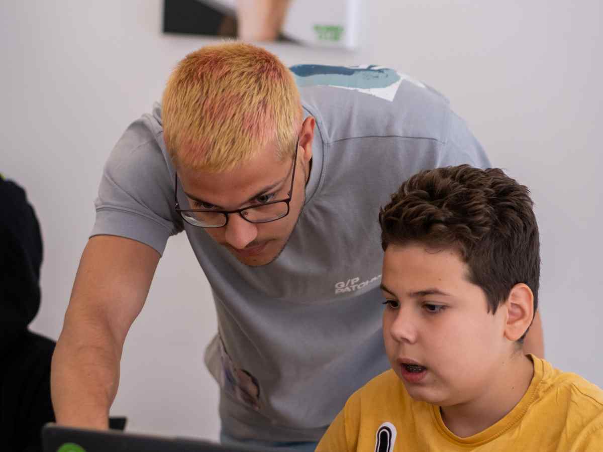 Trainer unterstützt ein Kind beim Roblox Workshop am Laptop.