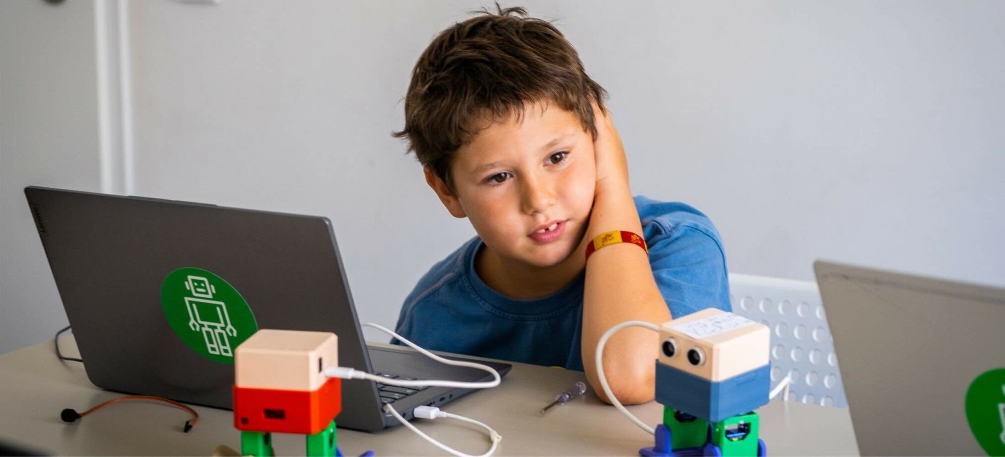 Ein Kind ab 7 Jahren programmiert im Robbo Club Feriencamp mit einem Laptop und arbeitet mit kleinen Robotern.