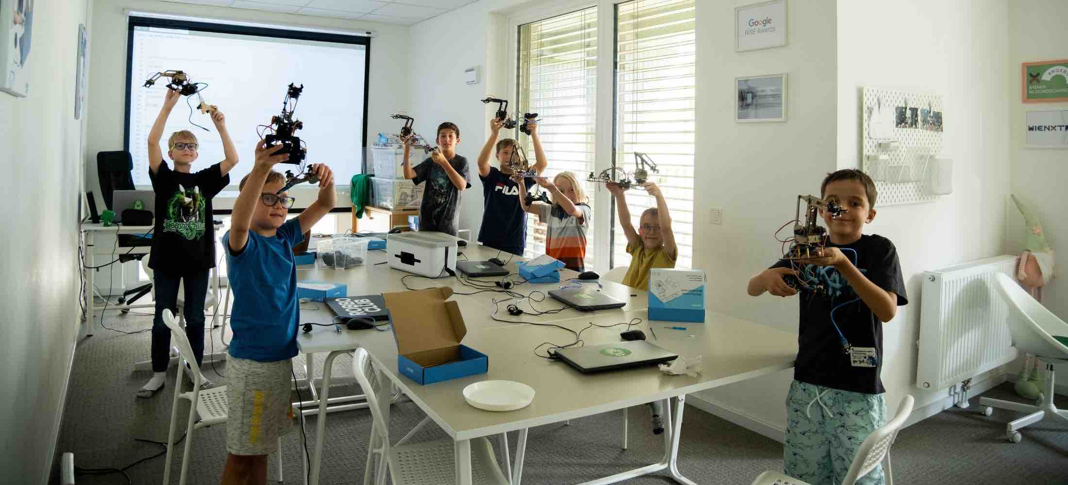 Kinder im Robbo Club halten ihre selbst programmierten Roboter hoch und präsentieren stolz ihre Projekte.