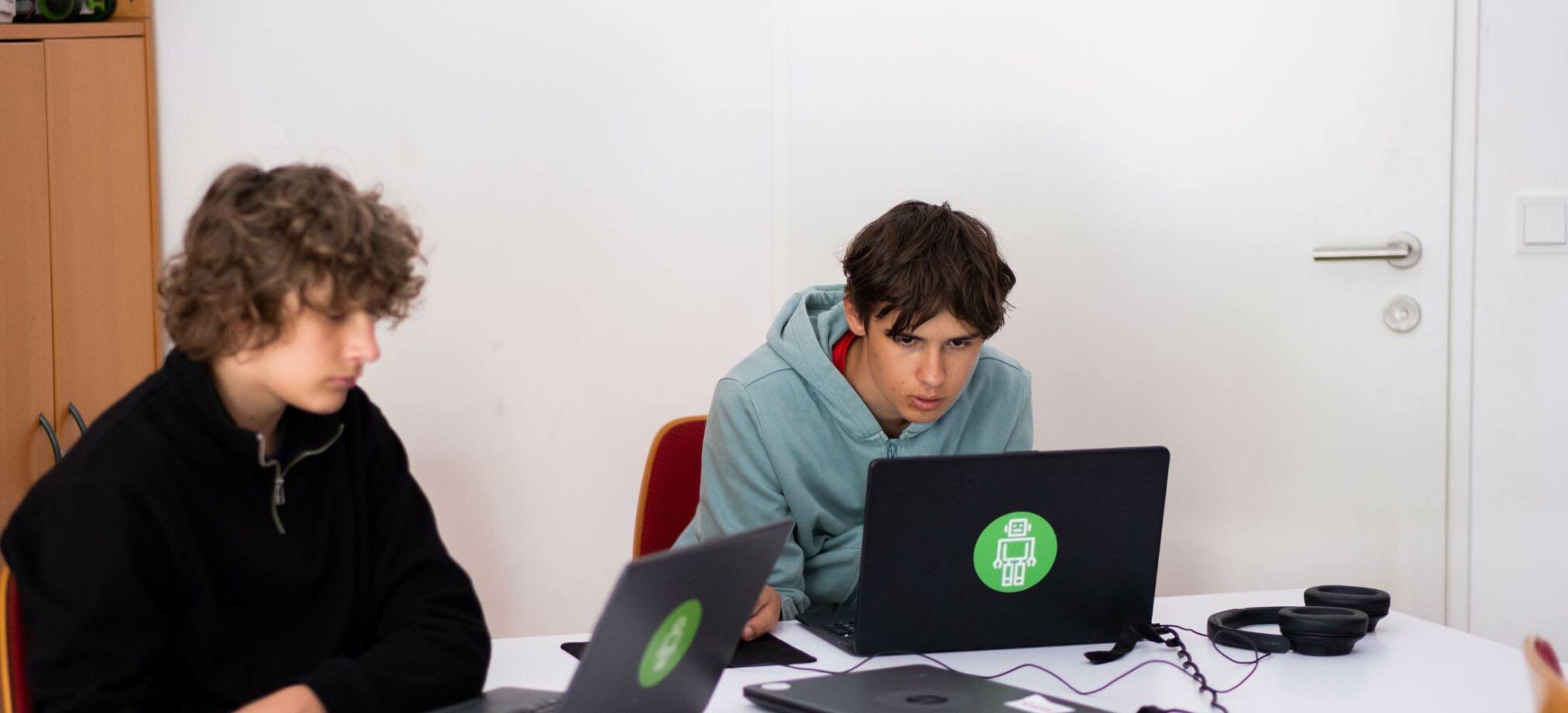 Jugendliche arbeiten konzentriert an Laptops im Robbo Club Feriencamp und entwickeln eigene Technik- und Coding-Projekte.