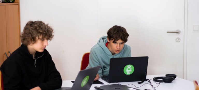 Jugendliche arbeiten konzentriert an Laptops im Robbo Club Feriencamp und entwickeln eigene Technik- und Coding-Projekte.
