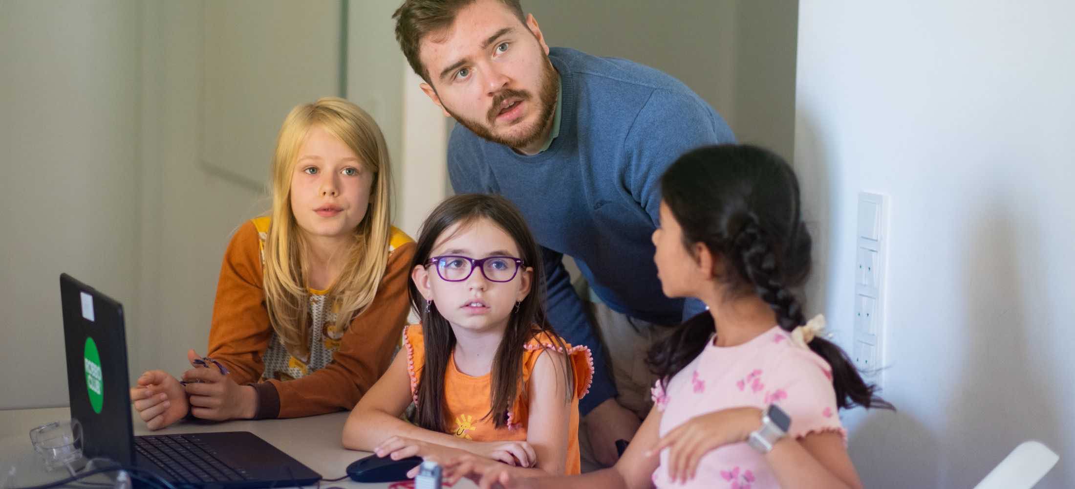 Kinder arbeiten gemeinsam mit einem Trainer an einem KI-Workshop im Robbo Club und lernen, wie künstliche Intelligenz funktioniert.