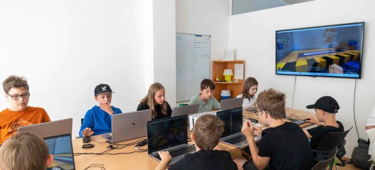 Kinder sitzen in einem Minecraft-Workshop des Robbo Clubs an Laptops und programmieren oder gestalten eigene Welten in Minecraft Education.