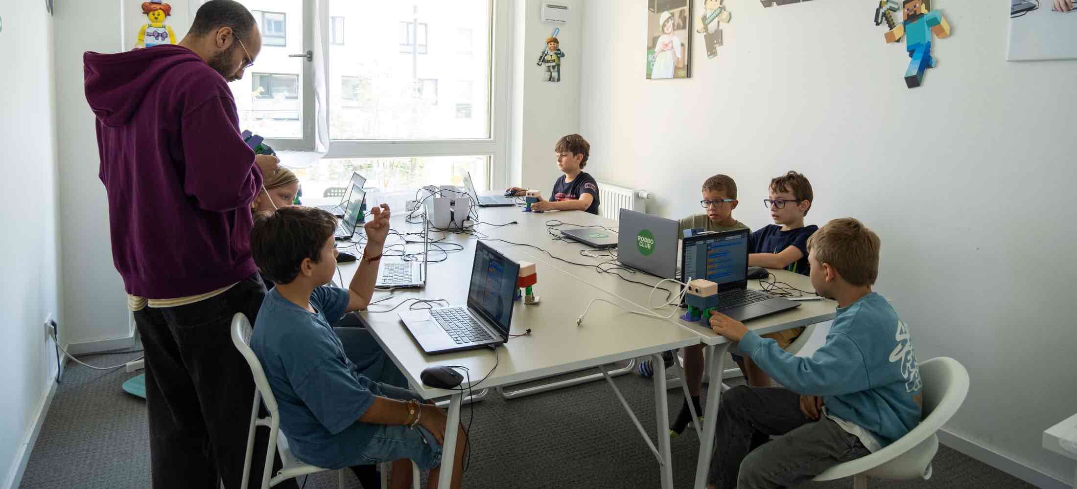 Kinder im Alter von 5 bis 7 Jahren arbeiten im Robbo Club mit einfachen Robotern und programmieren erste Bewegungen am Laptop.