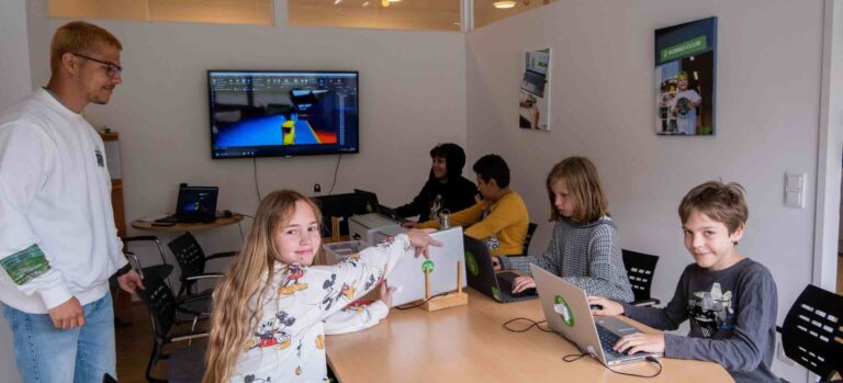 Kinder programmieren eigene Spiele im Roblox-Feriencamp des Robbo Club, unterstützt von einem Trainer.