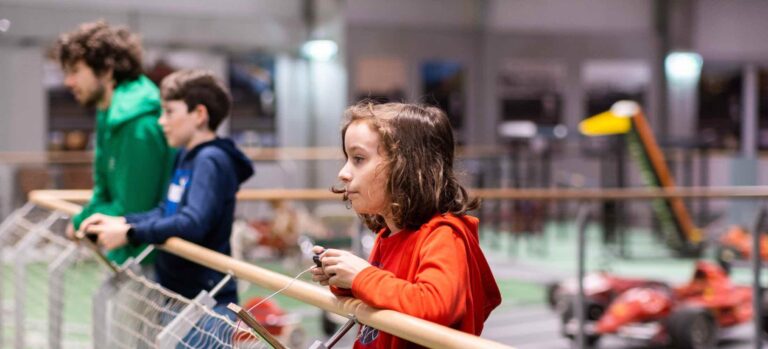 Kinder und Betreuer des Robbo Clubs beobachten eine technische Ausstellung und steuern Modelle während des Semesterferiencamps.