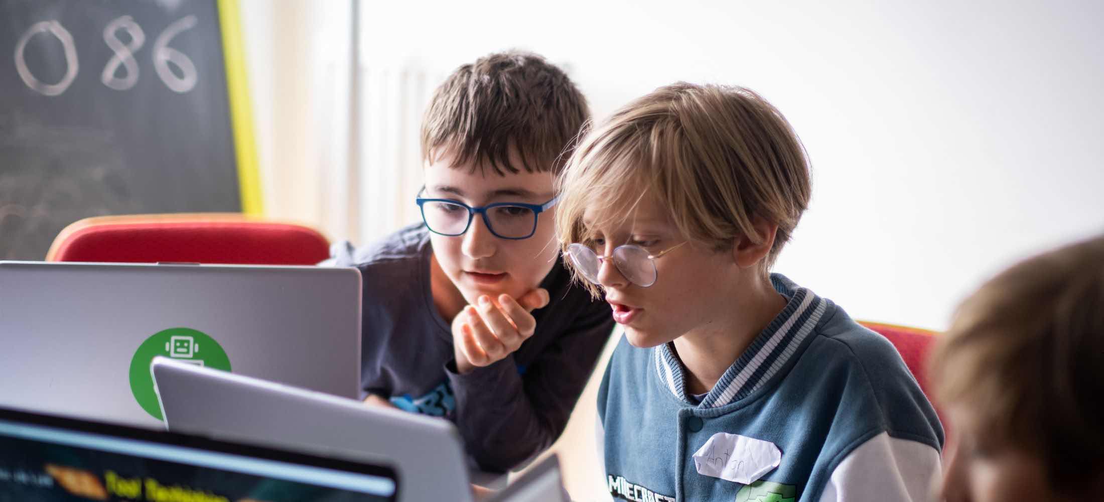 Zwei Kinder arbeiten gemeinsam am Laptop und tauschen sich während eines Weltspieltag-Workshops im Robbo Club über ihr Projekt aus.