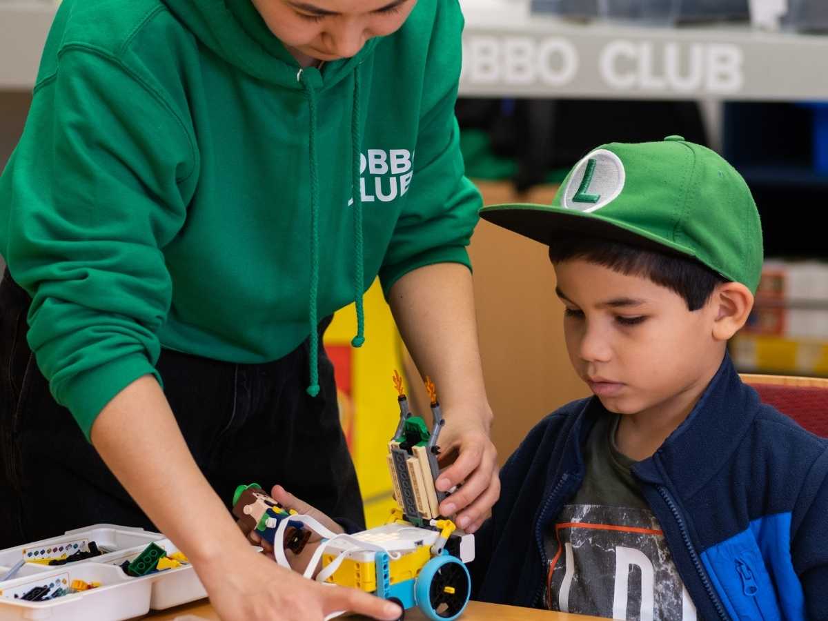 Kind baut Lego-Roboter mit Unterstützung eines Robbo Club Trainers