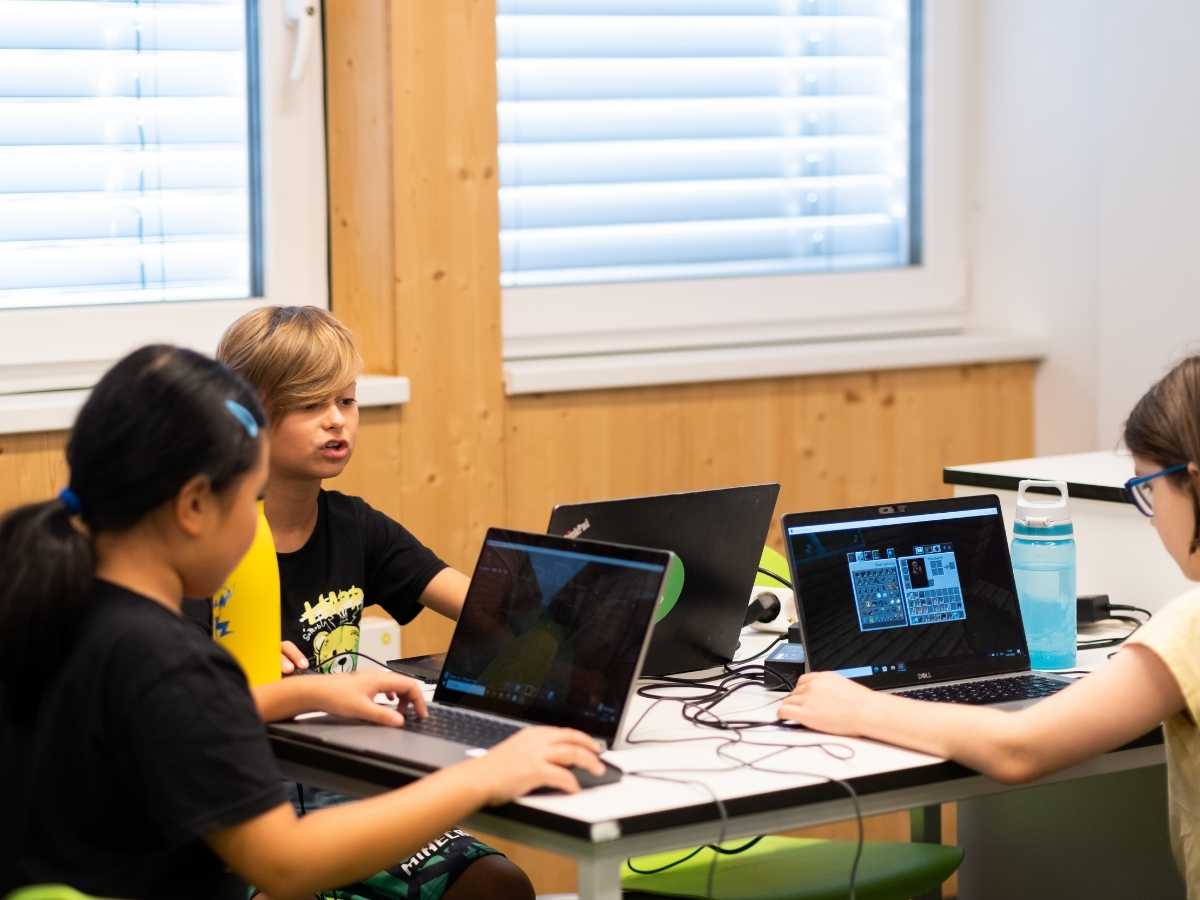 Kinder arbeiten gemeinsam an Laptops und lösen Programmieraufgaben im Team.