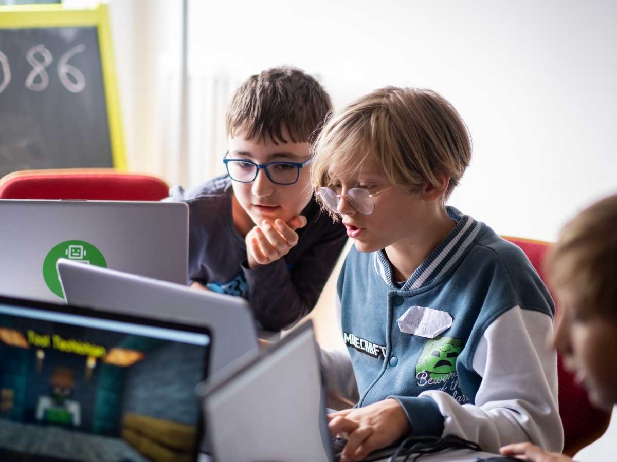 Zwei Kinder analysieren gemeinsam ein Programmierprojekt auf dem Laptop.