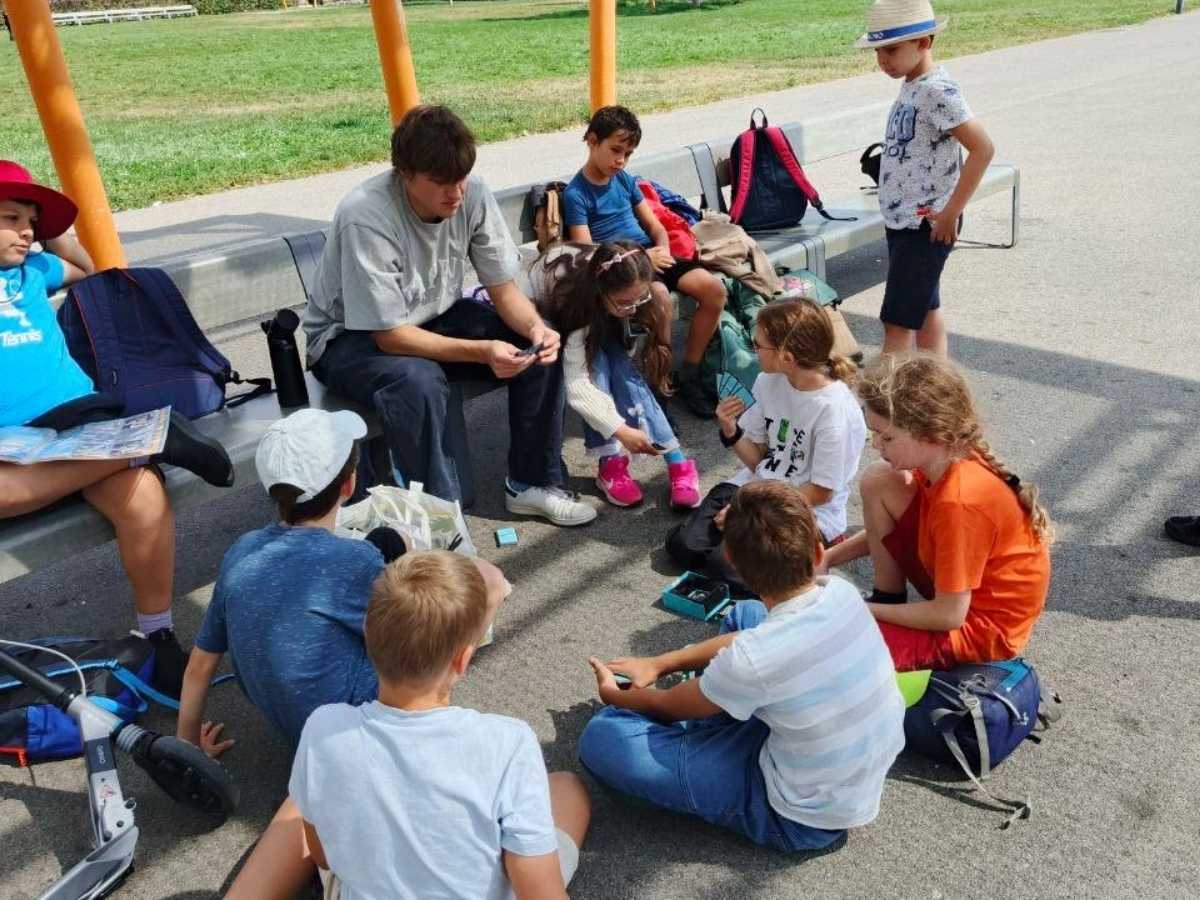Kinder hören einem Betreuer bei einer Outdoor-Erklärung im Feriencamp zu