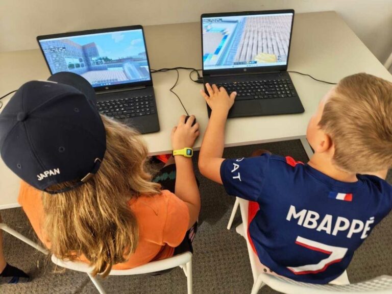 Zwei Kinder von hinten an Laptops, auf den Bildschirmen ihre Minecraft-Welten