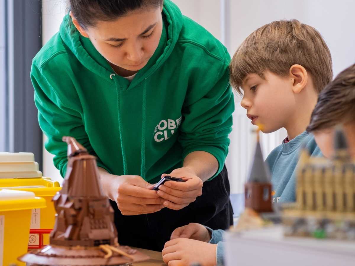 Betreuerin unterstützt ein Kind beim LEGO-Bauen im Robbo Club