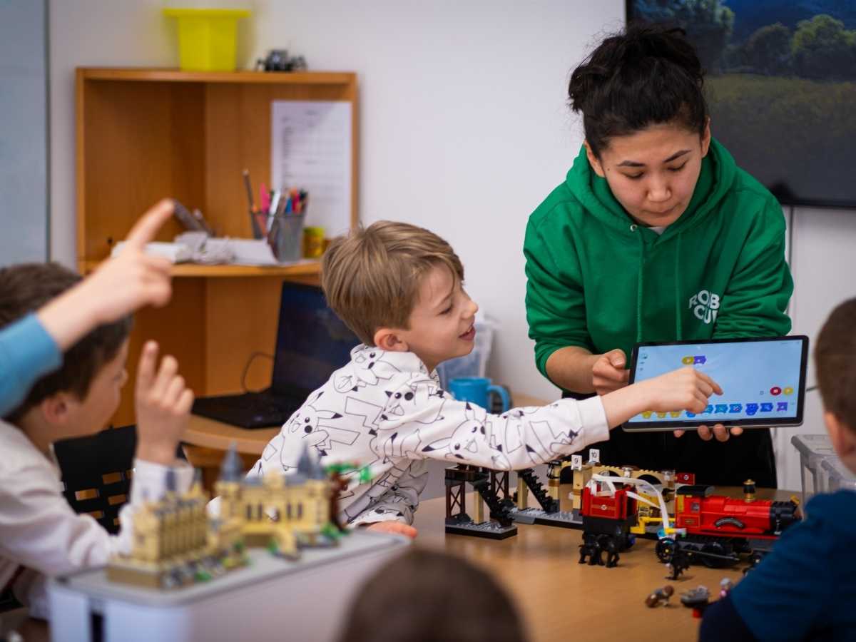 Trainerin erklärt Kindern die Programmierung einer LEGO Modellsteuerung.
