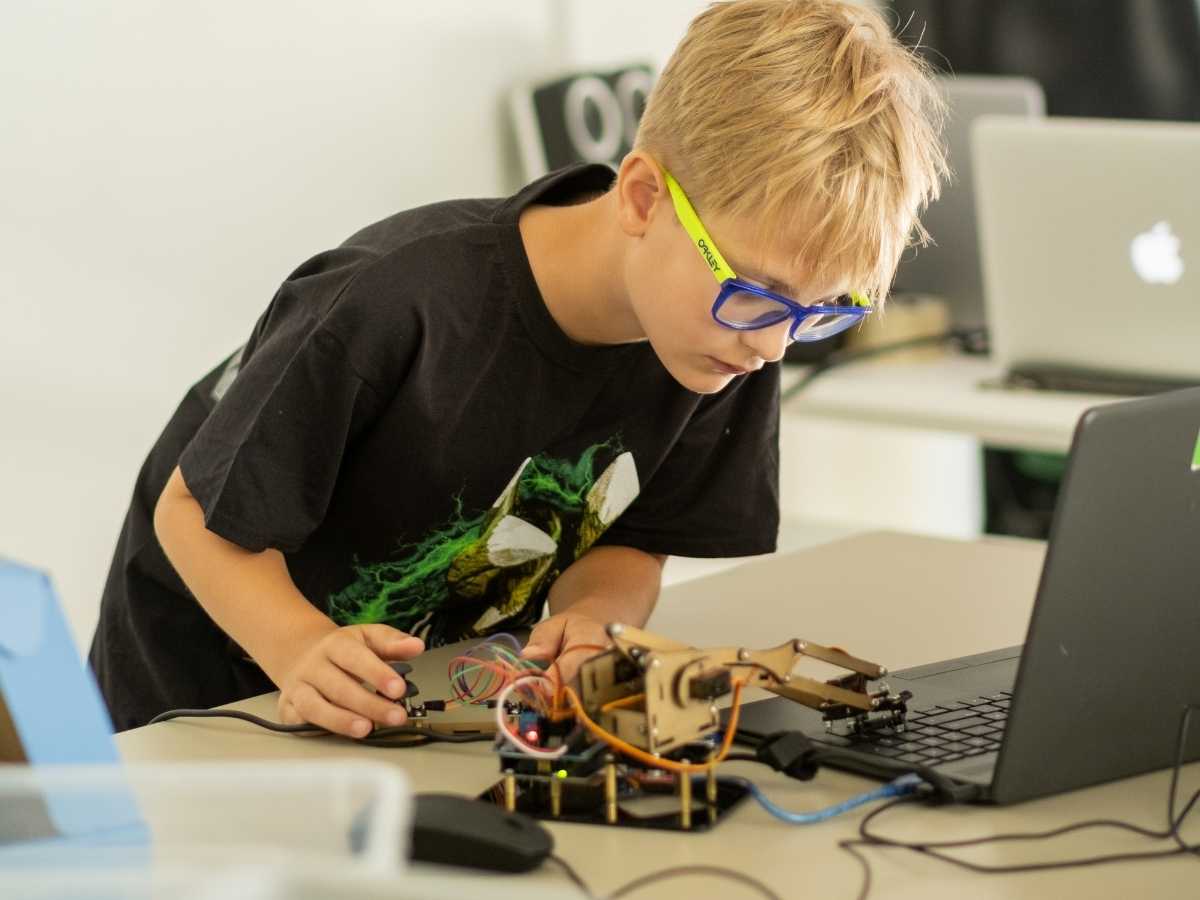 Junge programmiert einen Roboterarm mit Laptop im Technikunterricht