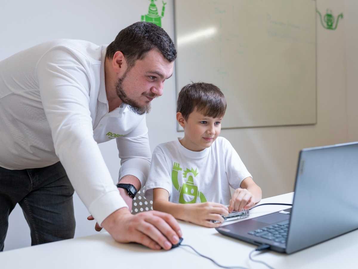 Trainer unterstützt Kind beim Programmieren am Laptop im Robbo Club