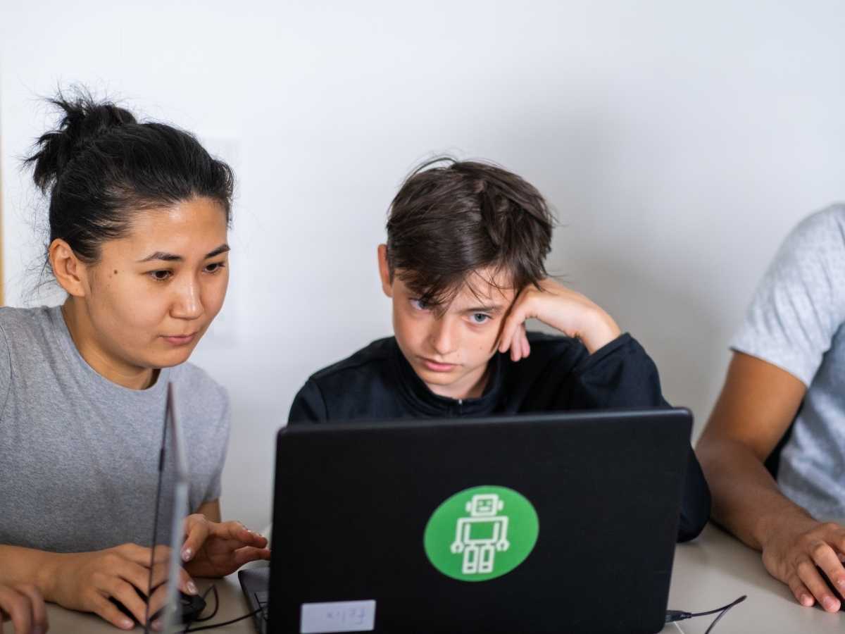 Mentorin unterstützt einen Jugendlichen beim Programmieren am Laptop im Robbo Club
