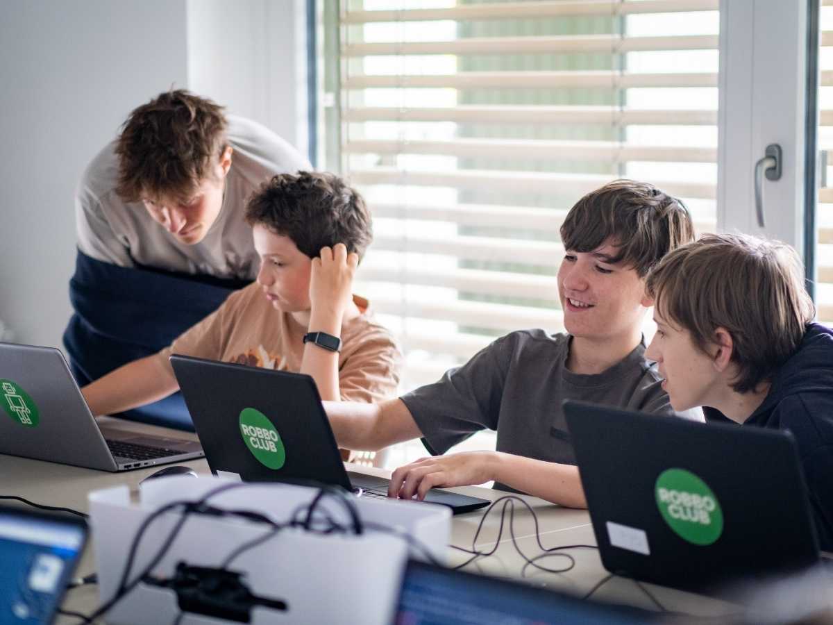 Jugendliche arbeiten gemeinsam an Laptops und besprechen Programmieraufgaben