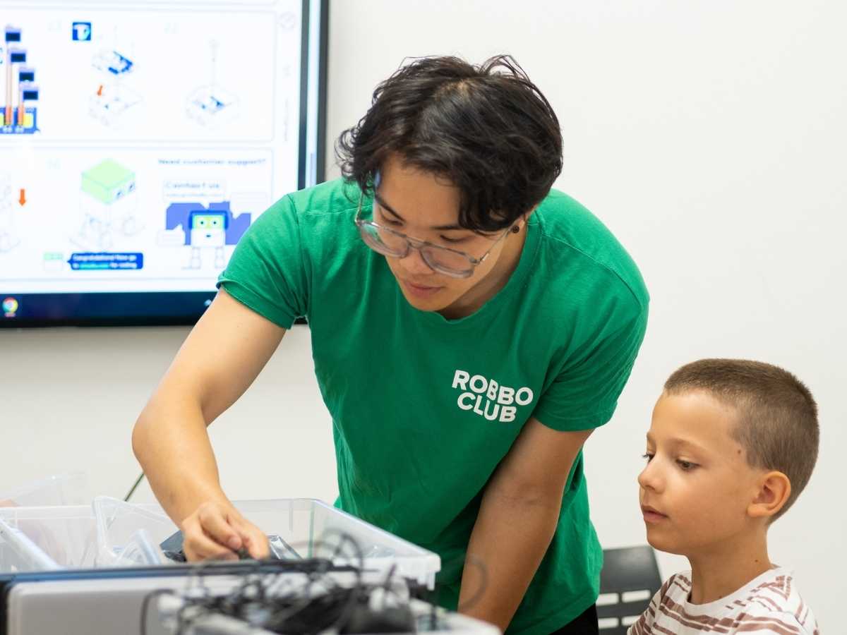 Trainerin unterstützt Kind bei der Auswahl von Technikmaterialien