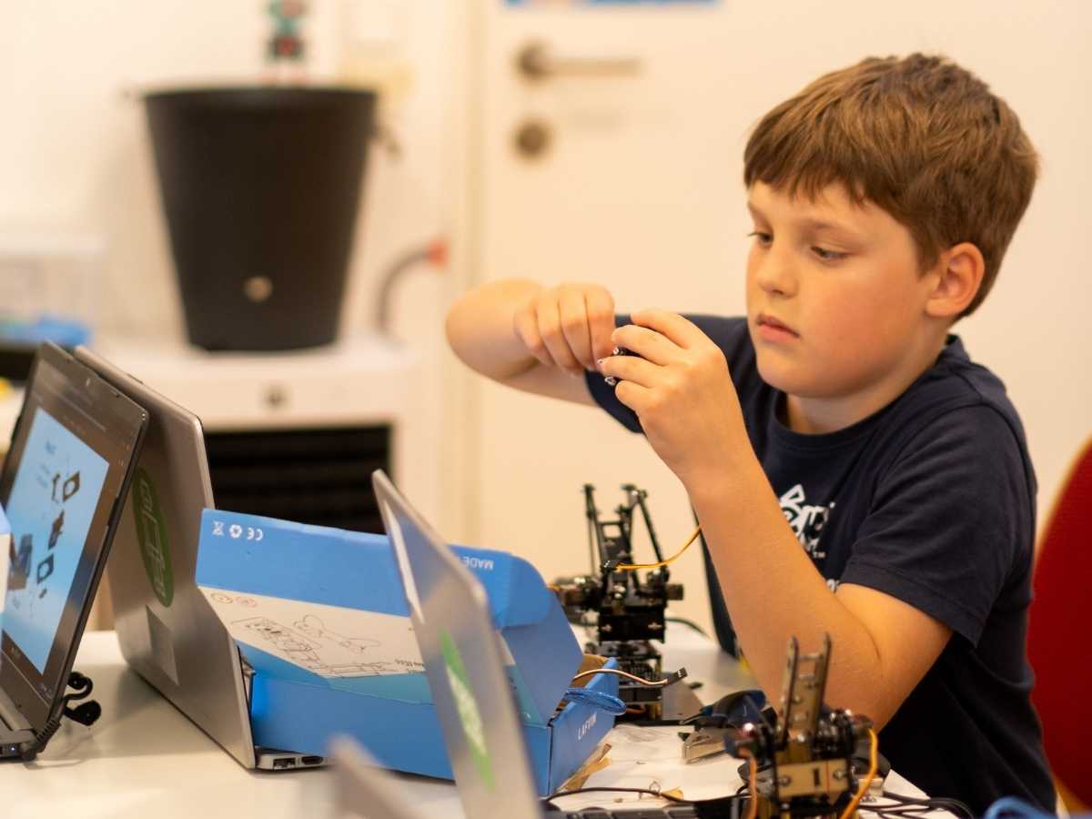 Kind baut einen Roboter mit Anleitung und Laptop im Robbo Club Wien
