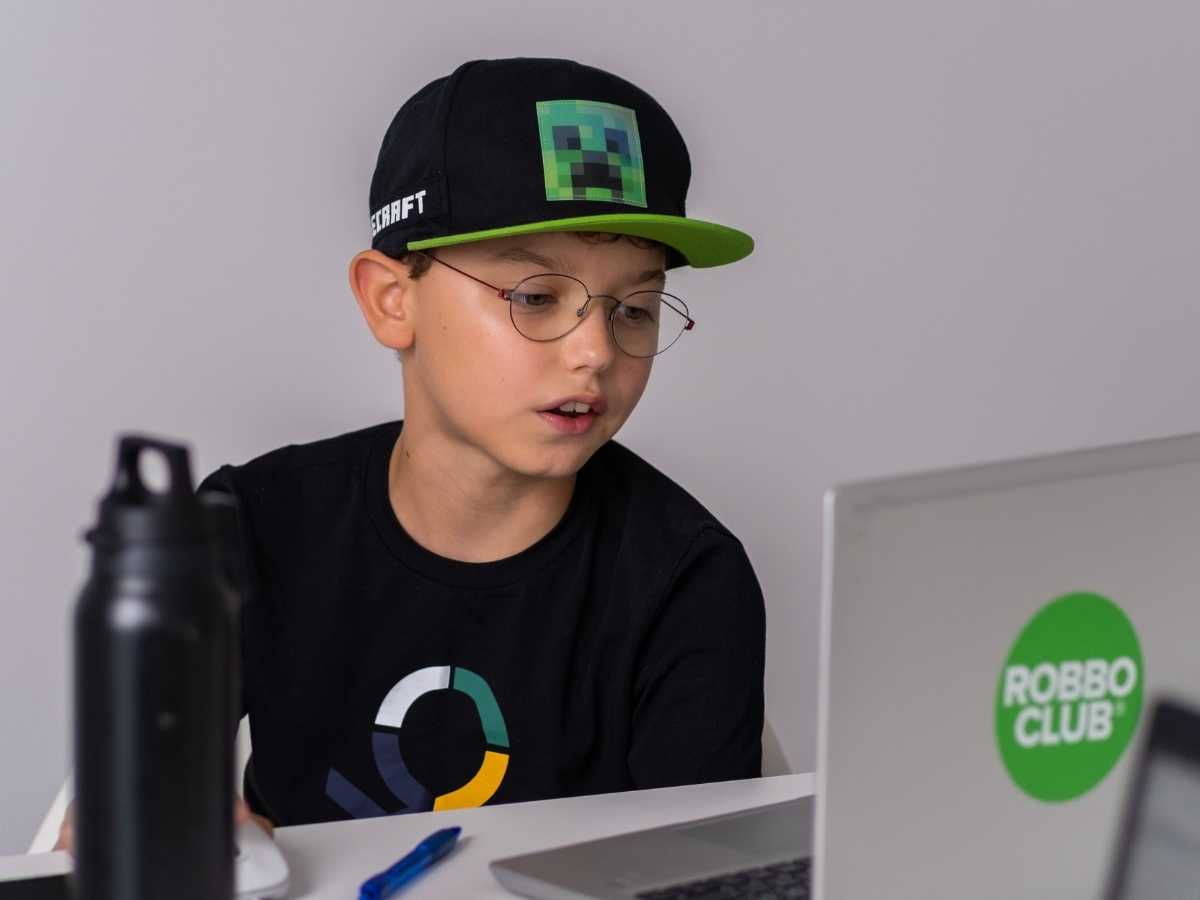 Junge mit Minecraft-Kappe arbeitet konzentriert am Laptop im Robbo Club