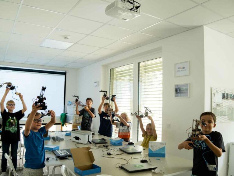 Gruppe von Kindern hält stolz ihre selbstgebauten Roboterarme in einem Robotikunterricht hoch.