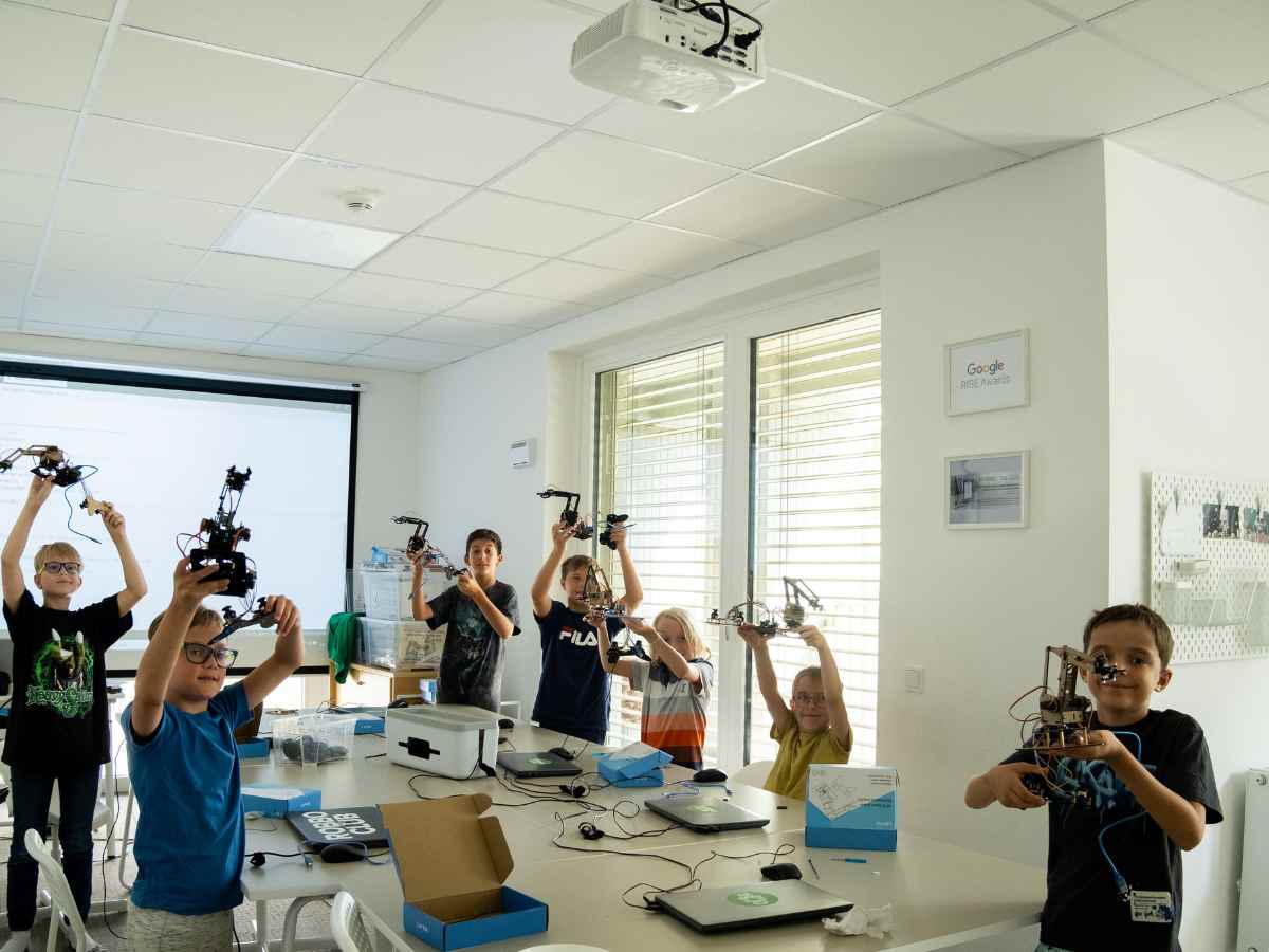 Gruppe von Kindern hält stolz ihre selbstgebauten Roboterarme in einem Robotikunterricht hoch.