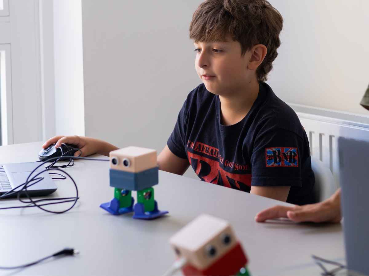 Junge programmiert einen kleinen zweibeinigen Lernroboter am Laptop.